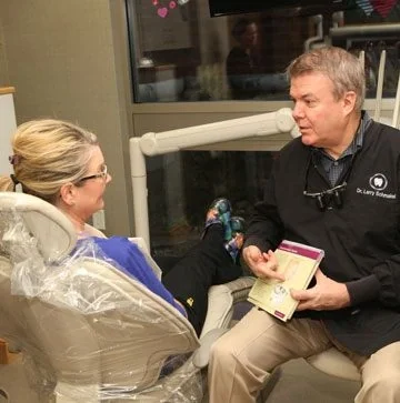 Dr. Larry Schmakel seated beside a patient in the chair, showing her a brochure.