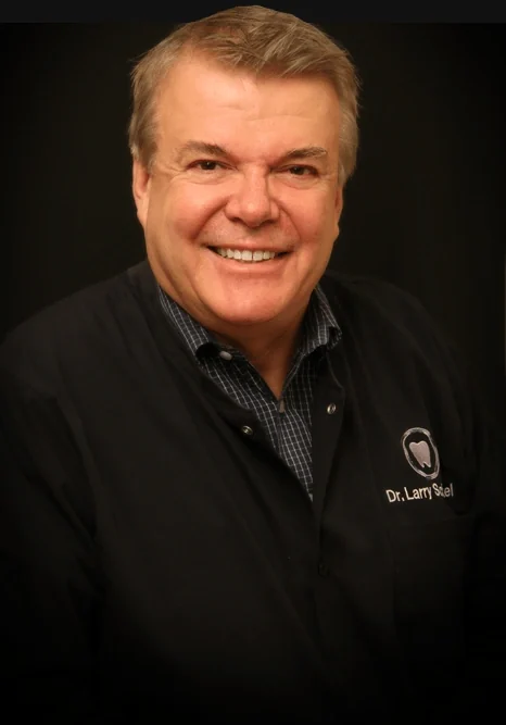 Dr. Larry Schmakel, DDS, smiling, in his black Sylvania Smile Design jacket.