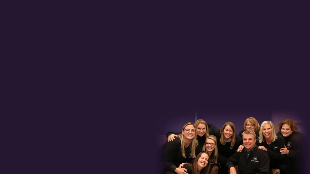 Dr. Larry Schmakel with the Sylvania Smile Design team, all in the practice's black jackets, gathered together and smiling.